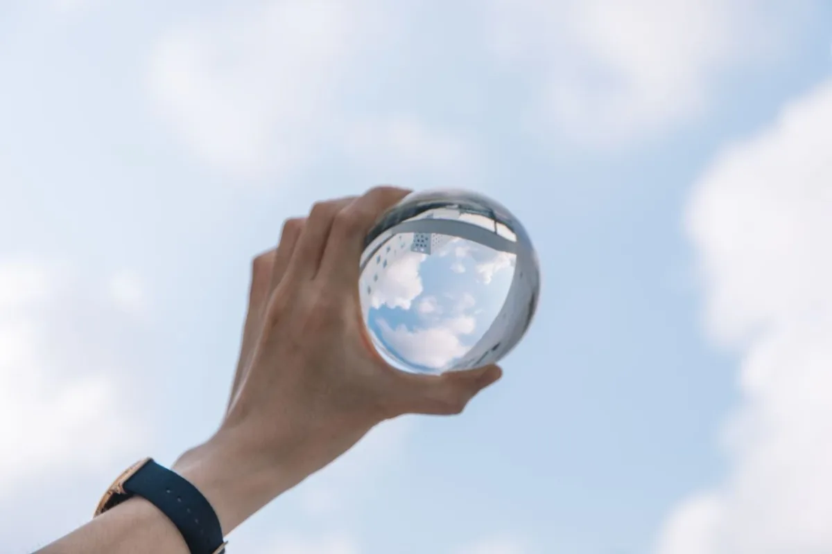 Hand met een glazen bol waarin de lucht weerspiegelt.