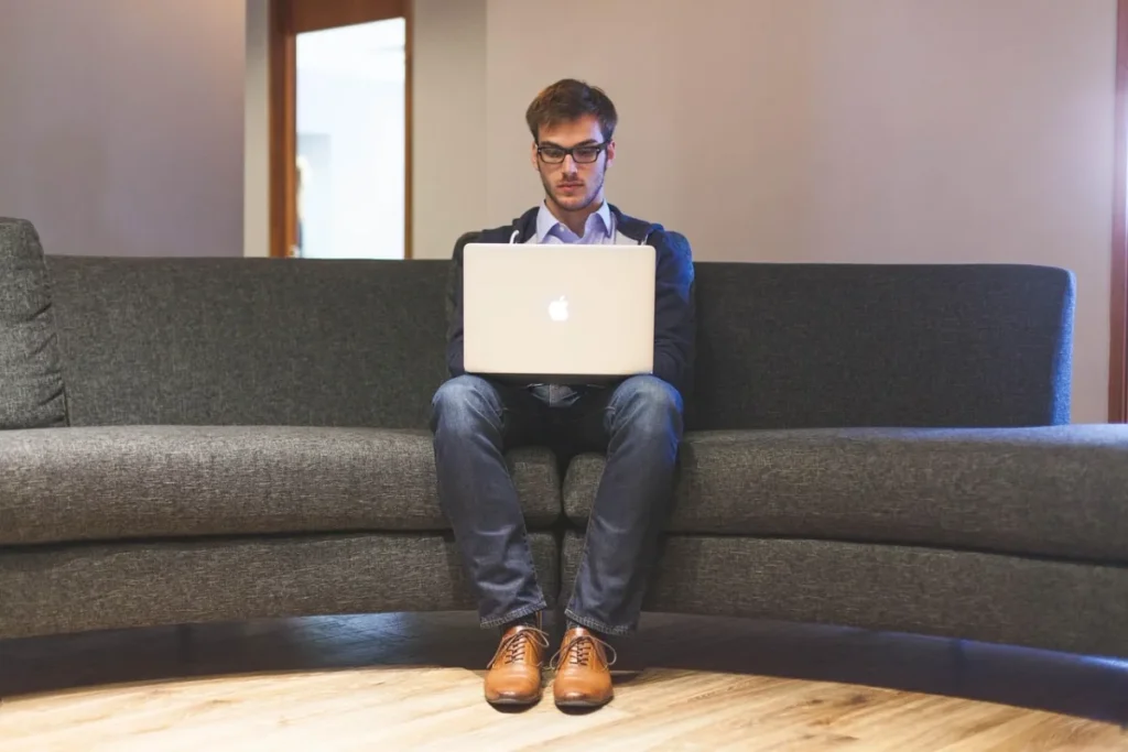 Man met een laptop op een bank in een kantoorruimte.